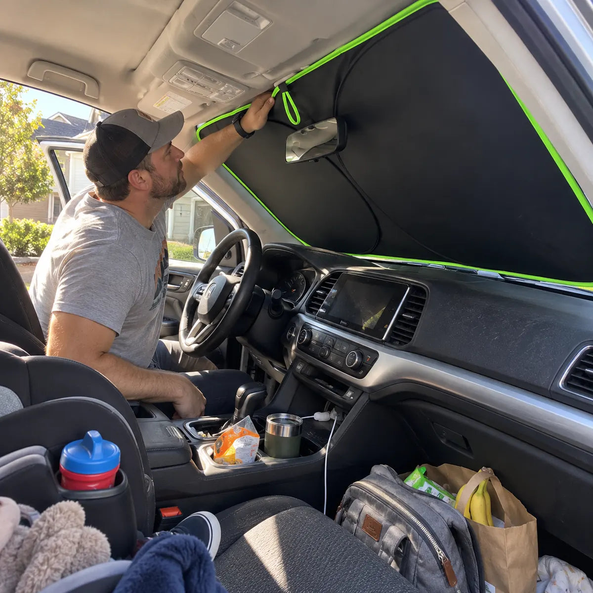 Driver installing a flexible windshield sun shade from inside the car