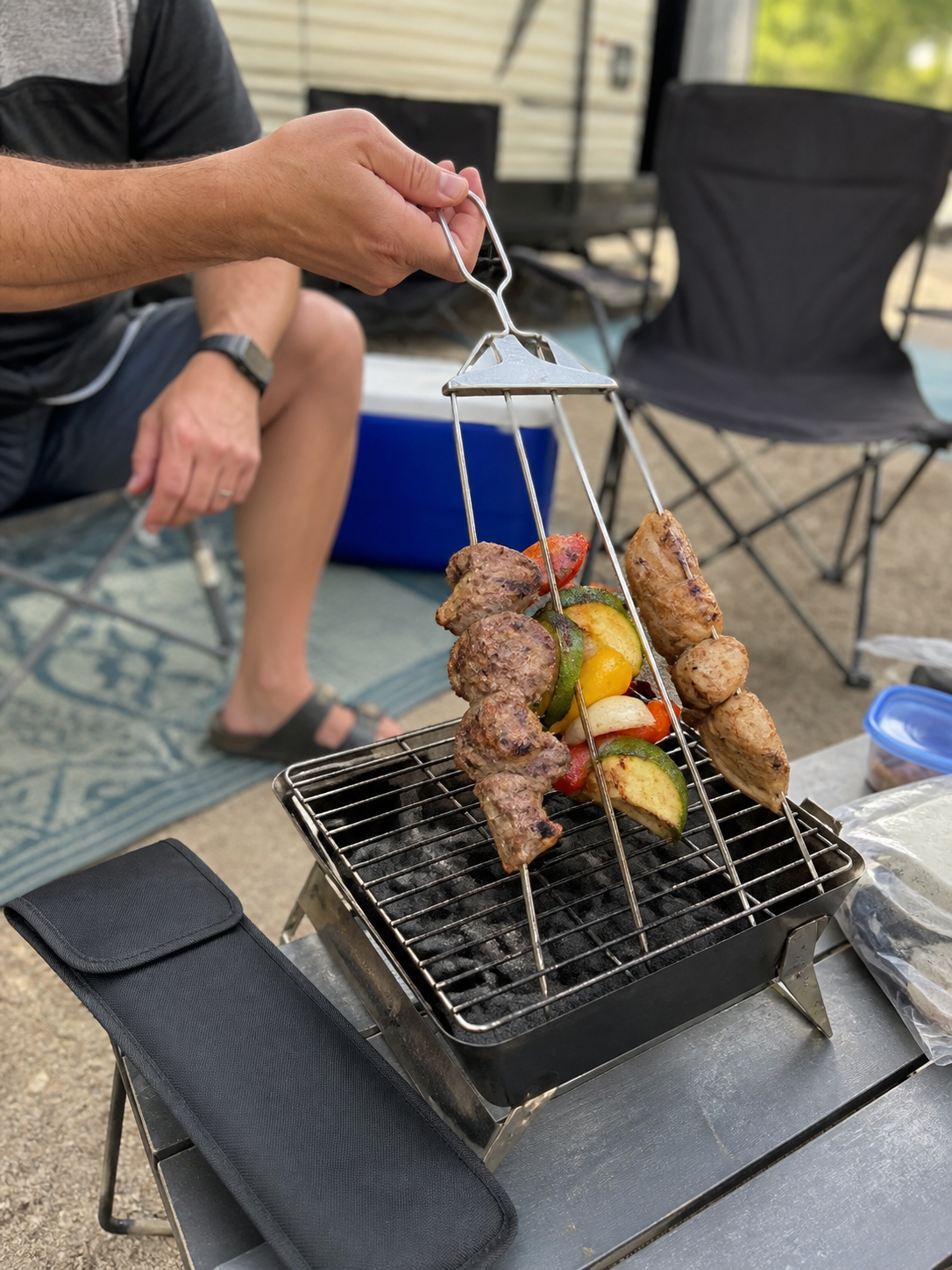 Camping grill user lifting 3-way skewers