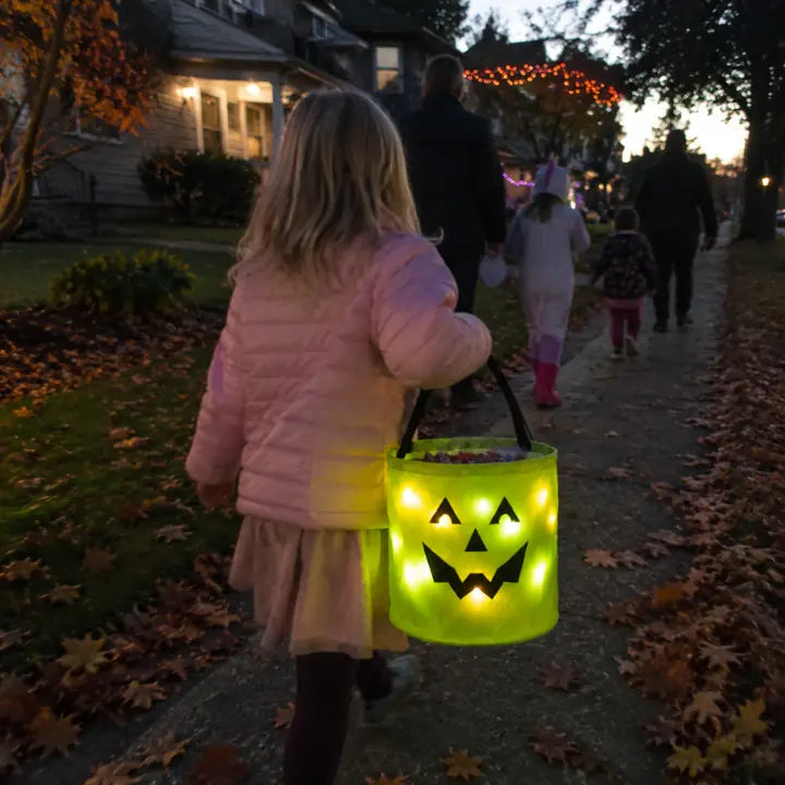 Child carrying a green BooLume light-up trick-or-treat bag on Halloween night