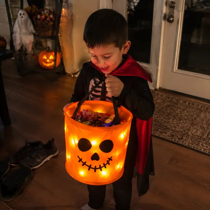 Child holding an orange BooLume light-up trick-or-treat bag at the door