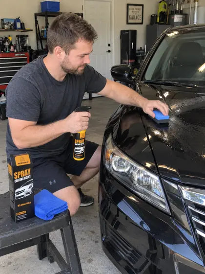 Customer applying car coating spray to a black car hood