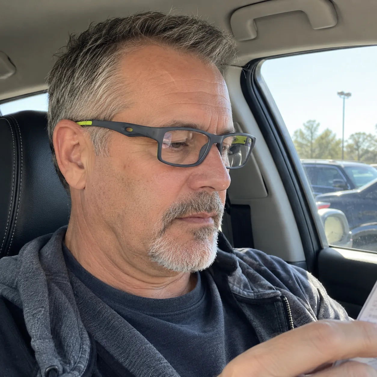 Customer wearing grey and green glasses while reading in a parked car