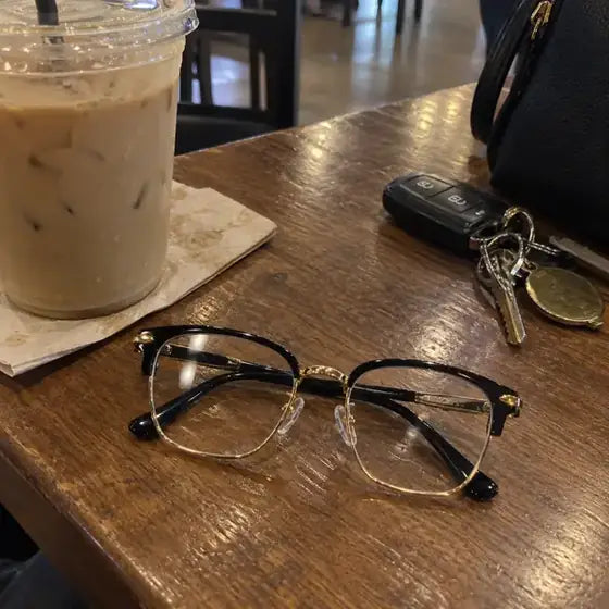 Black and gold glasses on a cafe table beside coffee and keys