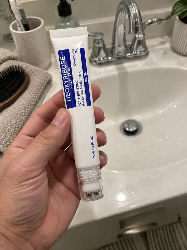 Hand holding scalp serum near a bathroom sink for daily use