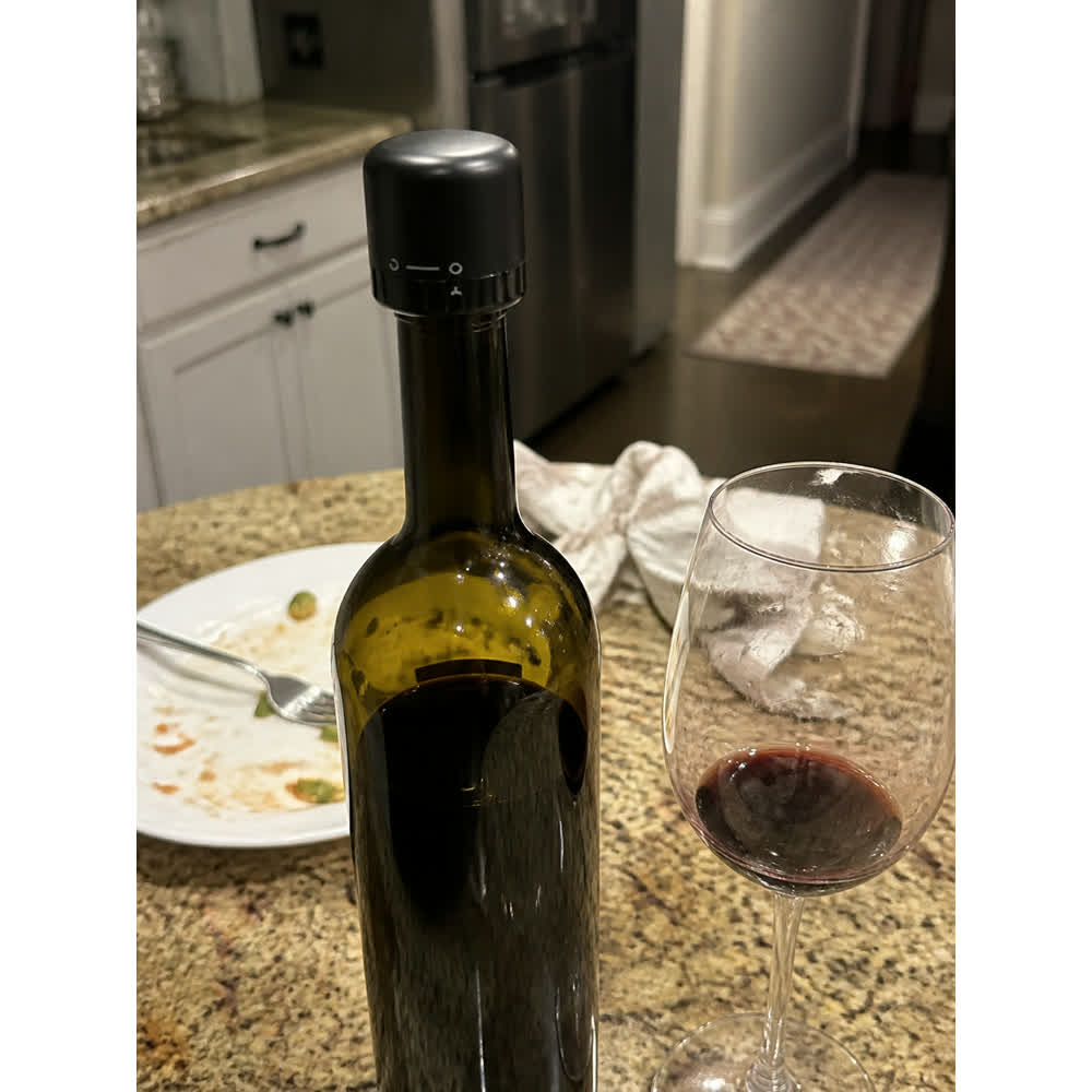Opened dinner wine bottle sealed with black wine stopper beside a wine glass
